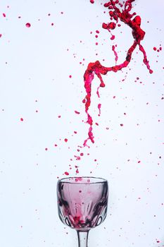 A splash of red wine in a glass on a white background. Cutout.