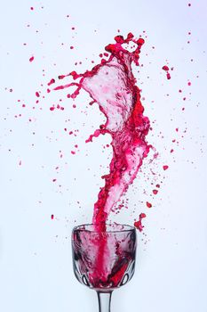A splash of red wine in a glass on a white background. Cutout.
