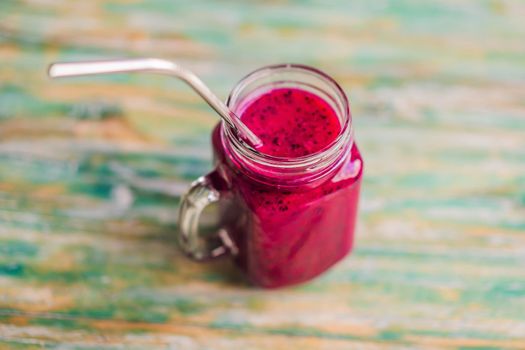 Dragon fruit smoothie with steel drinking straw on a painted wood background.