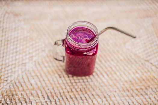 Dragon fruit smoothie with a steel drinking straw on a straw background.