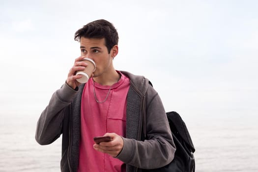 young man drinking coffee and using a mobile phone outdoors, concept of technology and communication, copy space for text