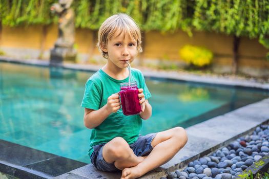 Boy drinks dragon fruit smoothie with steel drinking straw by the pool.