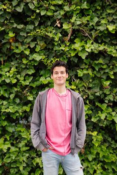 vertical photo of a friendly teenager smiling looking at camera on a green plants background, concept of human expressions and emotions, copy space for text