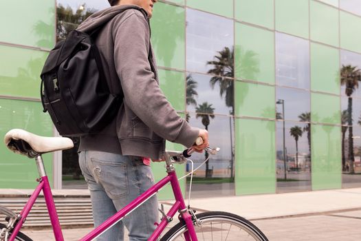 unrecognizable young man walking by the city with a retro bicycle, concept of sustainable urban transportation and ecological lifestyle, copy space for text