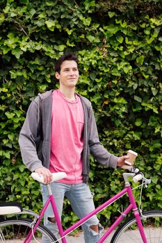 vertical photo of a happy young man smiling with a vintage bike on a green plants background, concept sustainable and ecological urban transportation, copy space for text