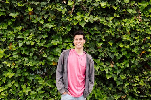 friendly teenager smiling looking at camera on a green plants background, concept of human expressions and emotions, copy space for text
