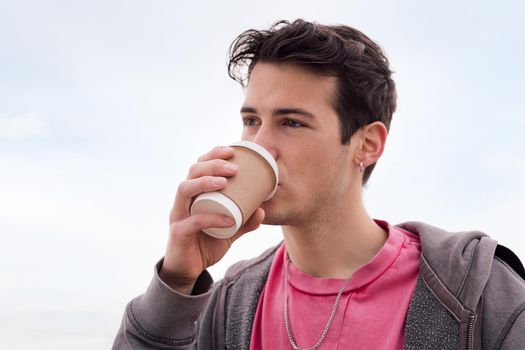 portrait of a handsome young student drinking a cup of coffee outdoors, concept of urban lifestyle, copy space for text
