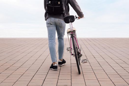 rear view of an unrecognizable young man walking while pushing a bicycle, concept of ecological and sustainable transportation, copy space for text