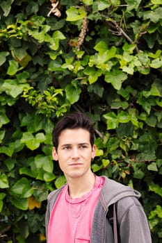 vertical photo of a handsome young teenager on a green plants background, concept of ecology and teenage lifestyle, copy space for text