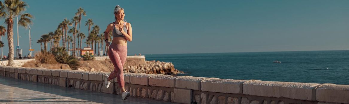 Strong female in sports top and pink leggings running near seashore and looking ahead on warm sunny day