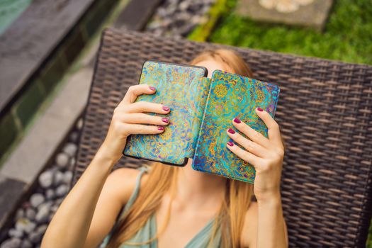 Woman reads e-book on deck chair in the garden.
