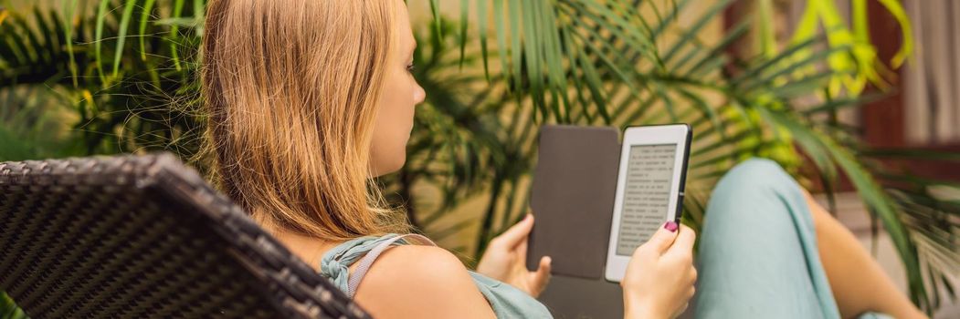 Woman reads e-book on deck chair in the garden. BANNER, LONG FORMAT