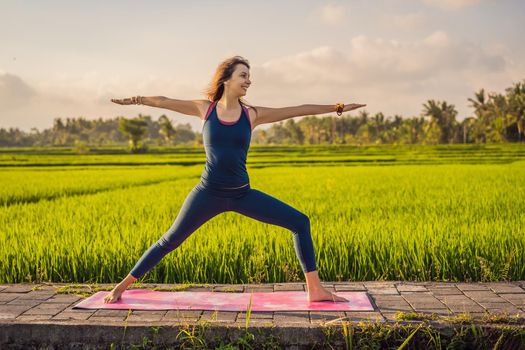 Young woman practice yoga outdoor in rice fields in the morning during wellness retreat in Bali.