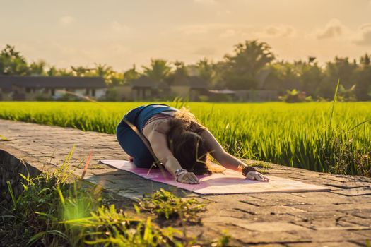 Young woman practice yoga outdoor in rice fields in the morning during wellness retreat in Bali.