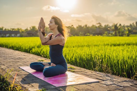 Young woman practice yoga outdoor in rice fields in the morning during wellness retreat in Bali.