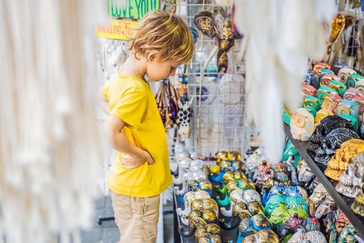 Boy at a market in Ubud, Bali. Typical souvenir shop selling souvenirs and handicrafts of Bali at the famous Ubud Market, Indonesia. Balinese market. Souvenirs of wood and crafts of local residents. Traveling with children concept. Kids friendly place.