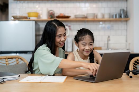 Mother teaching children to do their homework at home. Happy asian family using the laptop together at home. Young asian family parents helping daughter drawing at home.