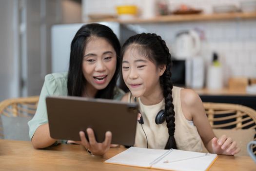 portrait of cheerful asian mother and daughter using digital tablet in kitchen at home.