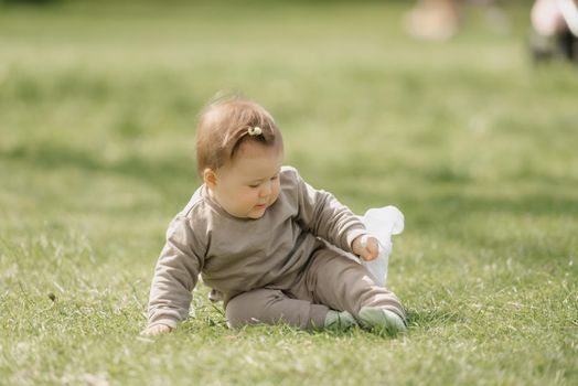 A smiling 7-month child is playing with a white panama hat in the meadow. An infant girl is crawling on the grass.