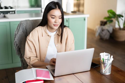 Young asian woman sitting at home with laptop, studying online, video chatting during school classes, doing homework or working remotely.