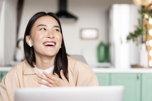 Happy asian woman at home relaxing with computer, laughing, watching videos on laptop.