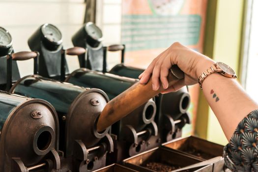Closeup on the hand of a Latin woman putting coffee to roast in a vintage manual machine