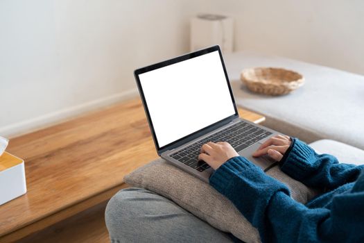 Top view mockup image of a woman working and typing on laptop computer with blank screen while sitting on a sofa at home.