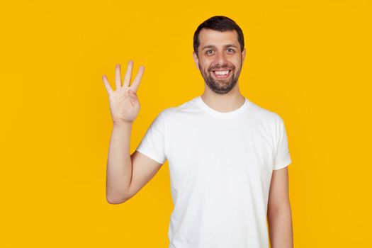 Modern young man with a beard in a white tank top shows number four with fingers on hand, smiling confidently and happily, looking at the camera The man shows four fingers. Number 4. yellow background