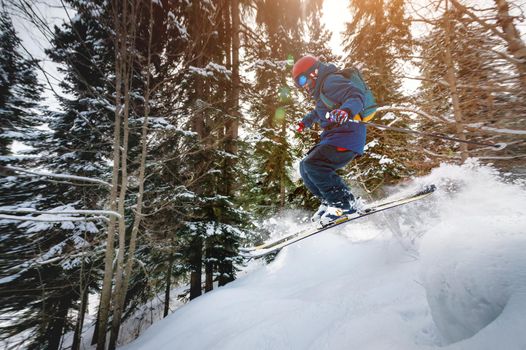 A male athlete skier rides a freeride in a winter forest in the mountains. Jump against the backdrop of snow-covered trees and the setting sun.