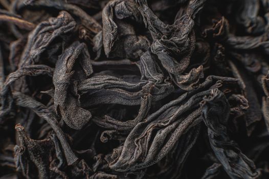 Black loose leaf tea as a background. Texture of dry black tea leaves. Dark background. Extreme macro mode. black leaf tea closeup.