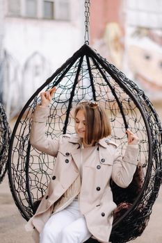 A happy stylish girl In a gray coat is sitting outside in an armchair.