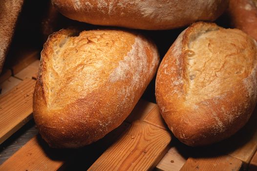 Fresh crispy hot delicious craft artisan bread. Many loaves lie on a wooden pallet.
