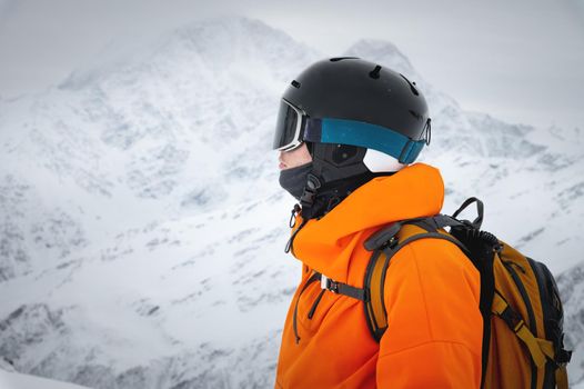 Portrait of a young adult in a ski helmet and goggles, with high snowy mountains in the background.