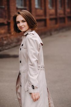 A happy stylish girl in a gray coat walks around the city.