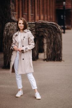 A happy stylish girl in a gray coat walks around the city.