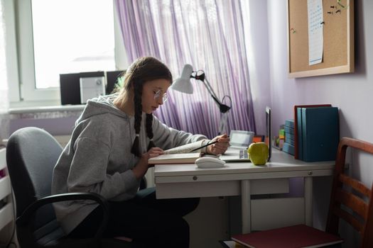 Reading a book. A student studies diligently from a book in her room. A capable schoolgirl. Young girl with braids.