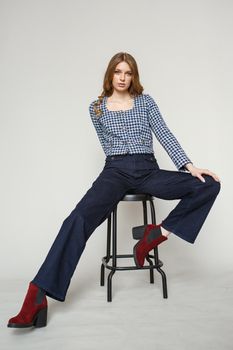 A girl in a denim suit standing on a studio background. The model is sitting on a chair