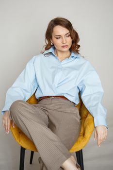 A girl in a blue shirt and trousers is sitting on a yellow chair.