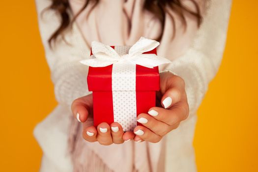 Happy young smiling woman holding and holding red gift box in front, offering and giving Christmas gifts. A girl in a sweater looks at the camera and gives a gift. Christmas New Year holiday concept