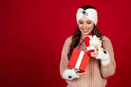 Happy young woman with a present, opening a Christmas present box. Portrait of happy smiling girl opening gift box isolated on red background