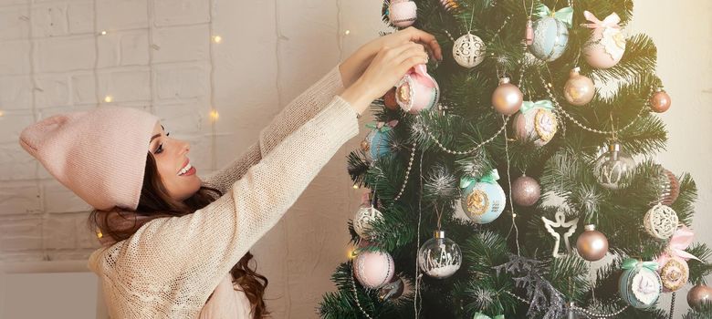 Happy young woman decorates the Christmas tree hang the ball on the tree. Christmas decoration, toys hanging on the tree, Christmas tree ball. New year and christmas holiday concept