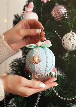 Close-up of female hands hang the ball on the tree. Christmas decoration, toys hanging on the tree, Christmas tree ball. New year and christmas holiday concept