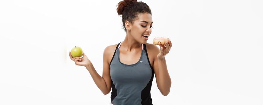 Healthy and diet concept - Beautiful sporty African American make a decision between donut and green apple. Isolated on white background