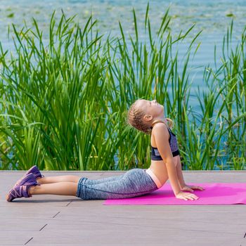 Little child is stretching on the grass at the shore of the lake.