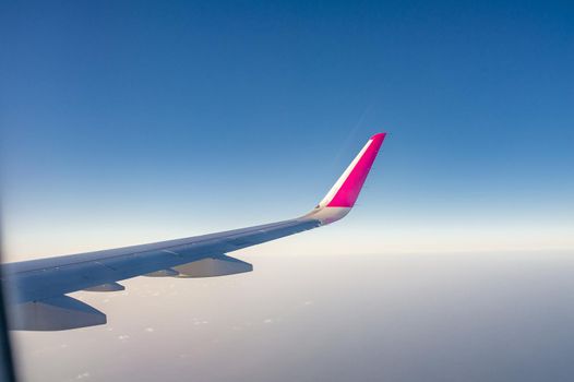 Picture taken from the plane through the window, you can see the blue sky and the wing cutting the air