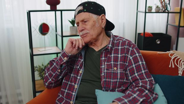 Portrait of sad senior old grandfather man sitting at home looks pensive thinks over lonely life or problems, crisis, suffers from unfair situation. Illness, anxiety, depressed, feeling bad annoyed