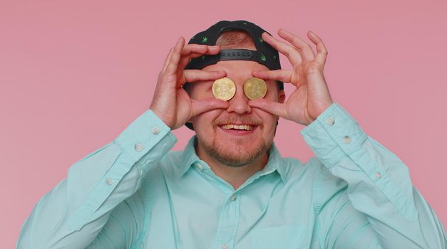 Happy man winner showing golden bitcoins. Career wealth, cryptocurrency investment, mining future technology. Young adult guy fooling making faces. Happy businessman isolated on pink studio background