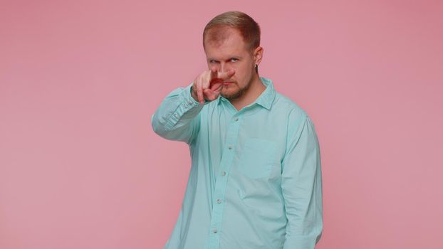 I am watching you. Man in blue casual shirt pointing at his eyes and camera, show I am watching you gesture, spying on someone. Young adult blonde guy boy isolated alone on pink studio wall background