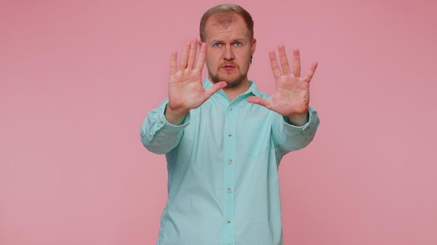 No stop. Serious adult man say no, hold palm folded crossed hands in stop danger gesture, warning of finish, prohibited access, declining communication, body language. Young one guy on pink background