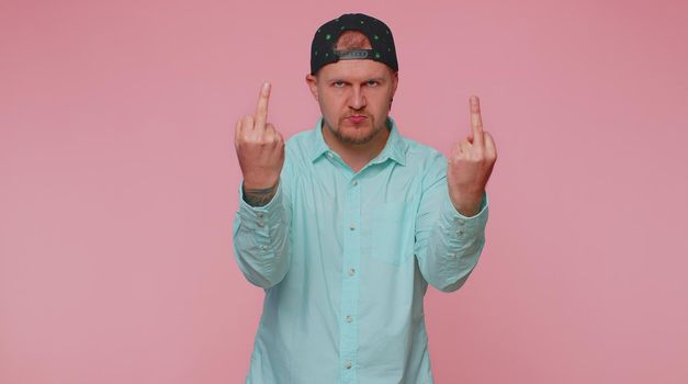 Aggressive crazy hooligan one man showing around his middle fingers, demonstrating protest with impolite rude gesture of disrespect, rejecting communication. Young guy isolated on pink background